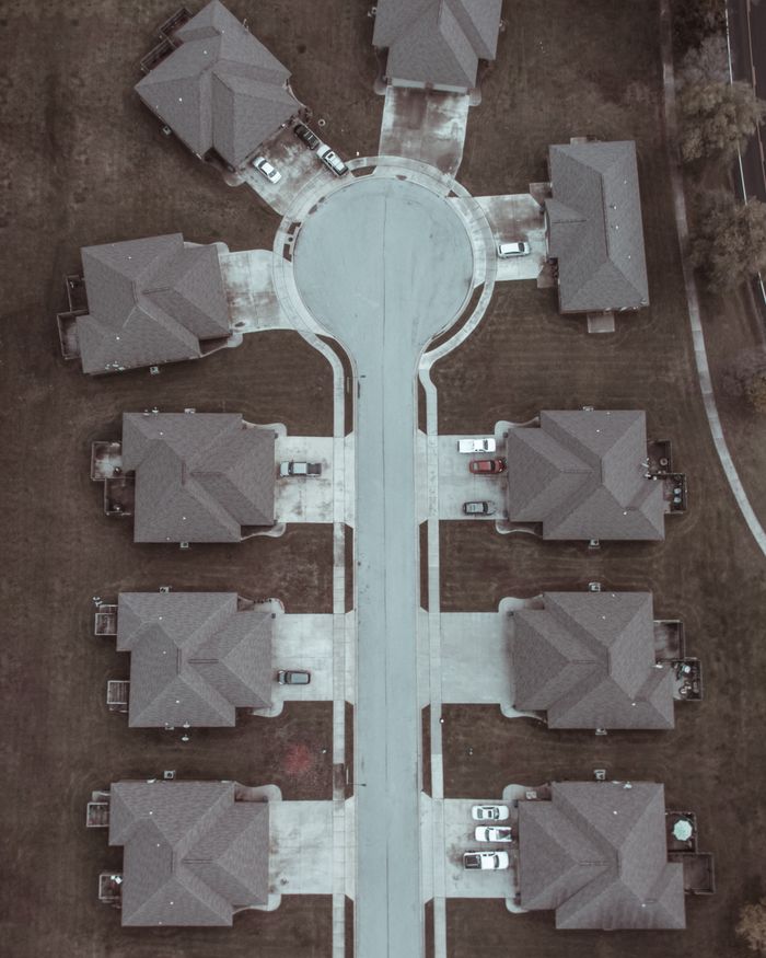 who-we-are Aerial shot of a suburban cul-de-sac with identical houses and parked cars.