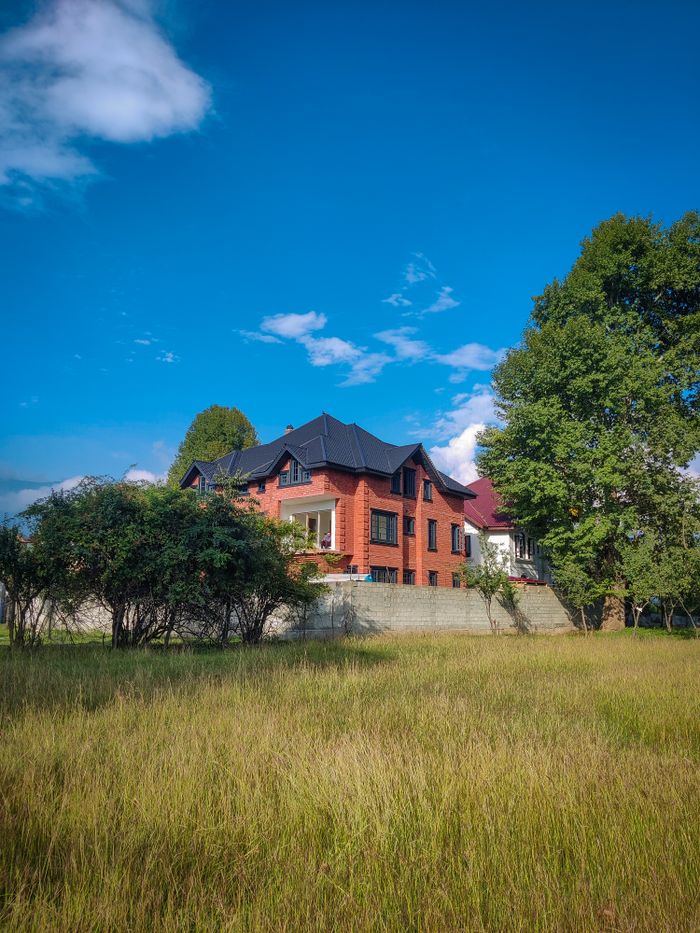 services-01 Red brick house behind trees under clear blue sky, surrounded by nature